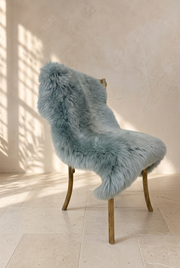 Ash grey sheepskin draped over a wooden chair in a warm neutral interior