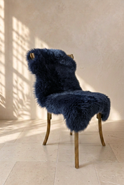 Navy blue sheepskin draped over a wooden chair in a warm neutral interior