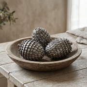Three silver decorative pine cones styled in a rustic wooden bowl